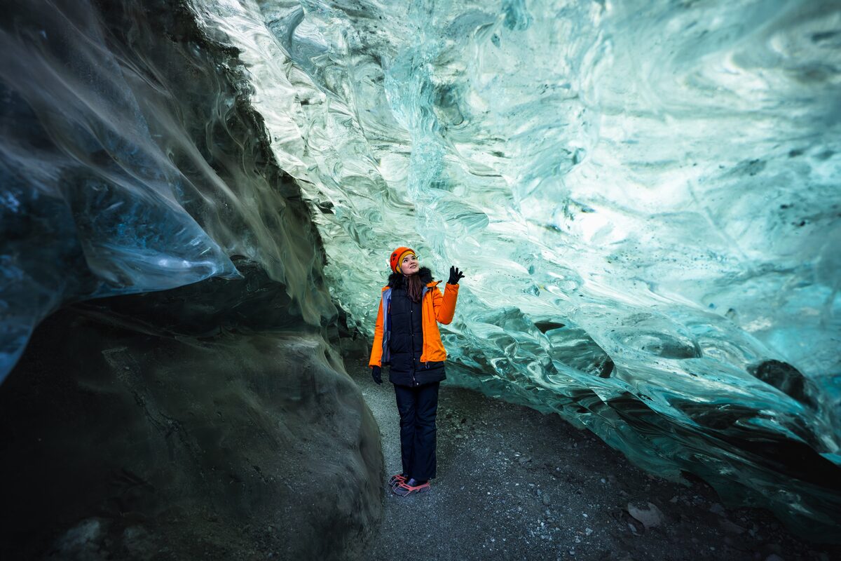 Woman In An Orange Jacket Smiling At Crystal Ice Cave in iceland