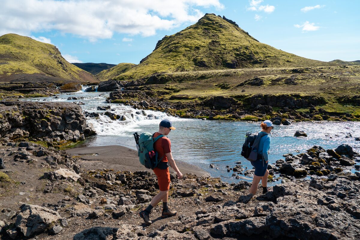 People Hiking Near A River With Hills In The Background in Iceland