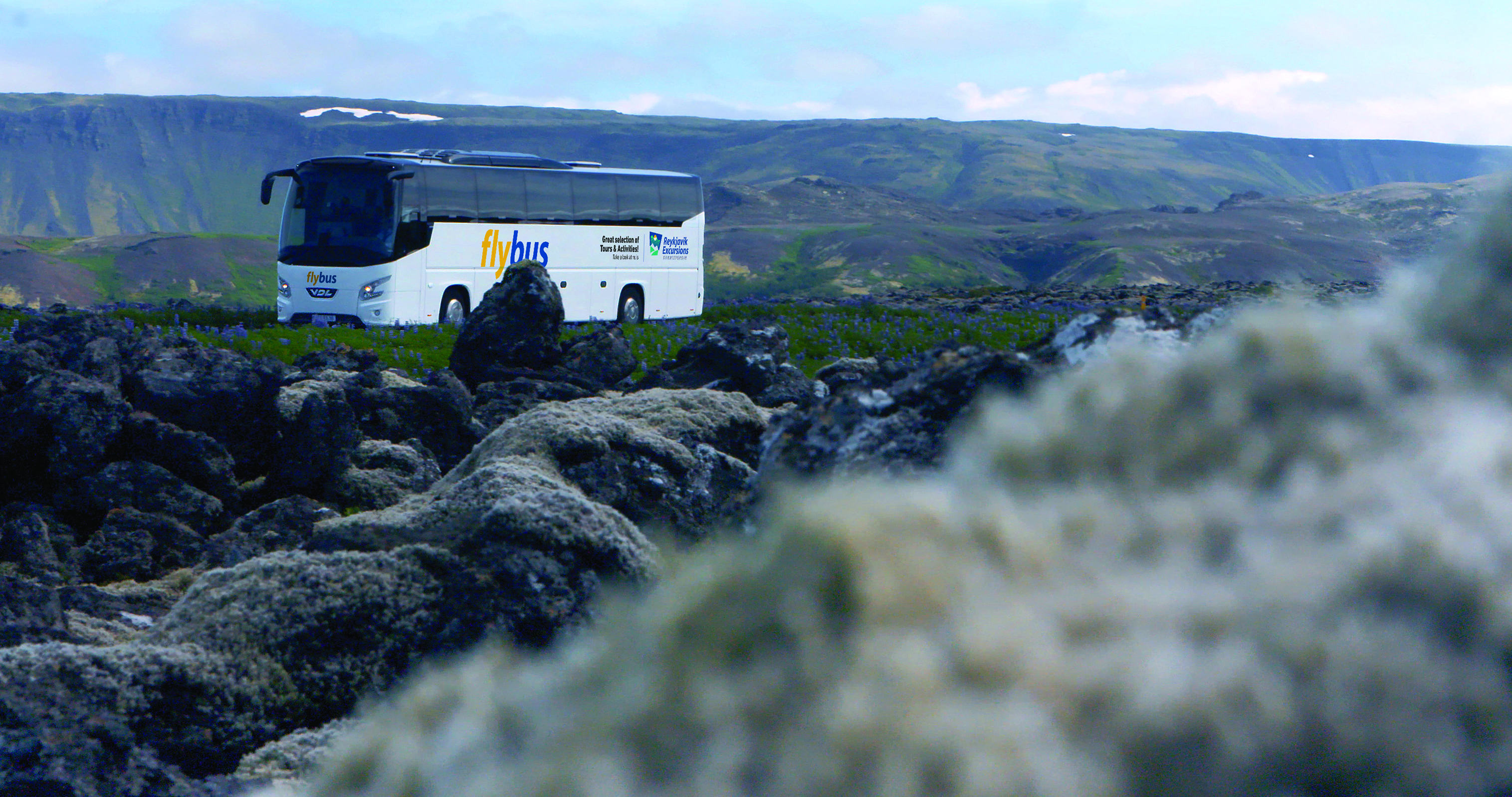 Flybus Bus Driving With Rocks And Mountains Surrounding It in Iceland