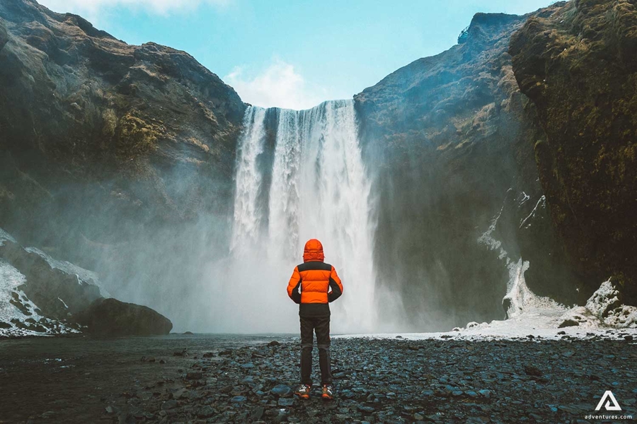 Man Standing In Front Of Skogafoss Waterfall In South Coast Iceland