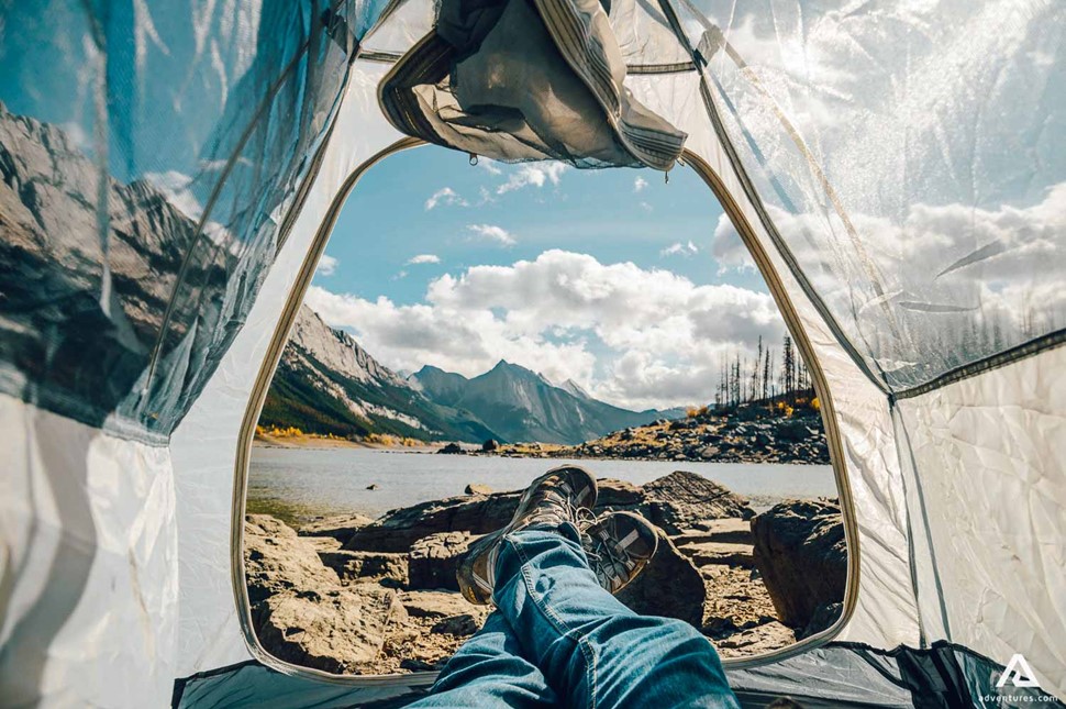 Man Lying In A Tent In Front Of Medicine Lake In Canadian Rockies