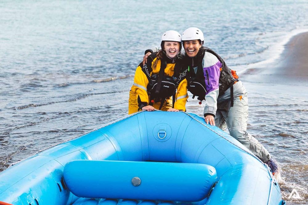 Two Girls Are Smiling Next To Rafting Boat By River