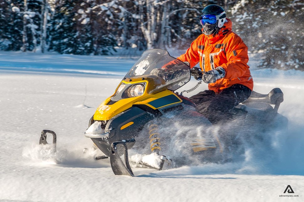 Man with orange jacket sitting on snowmobile
