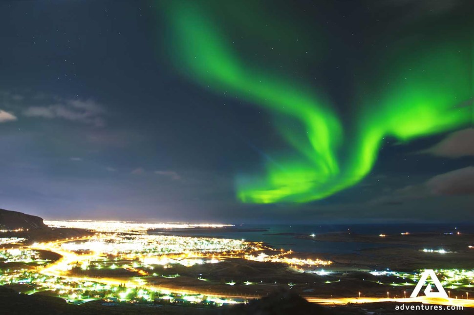 northern lights above bright city lights in iceland